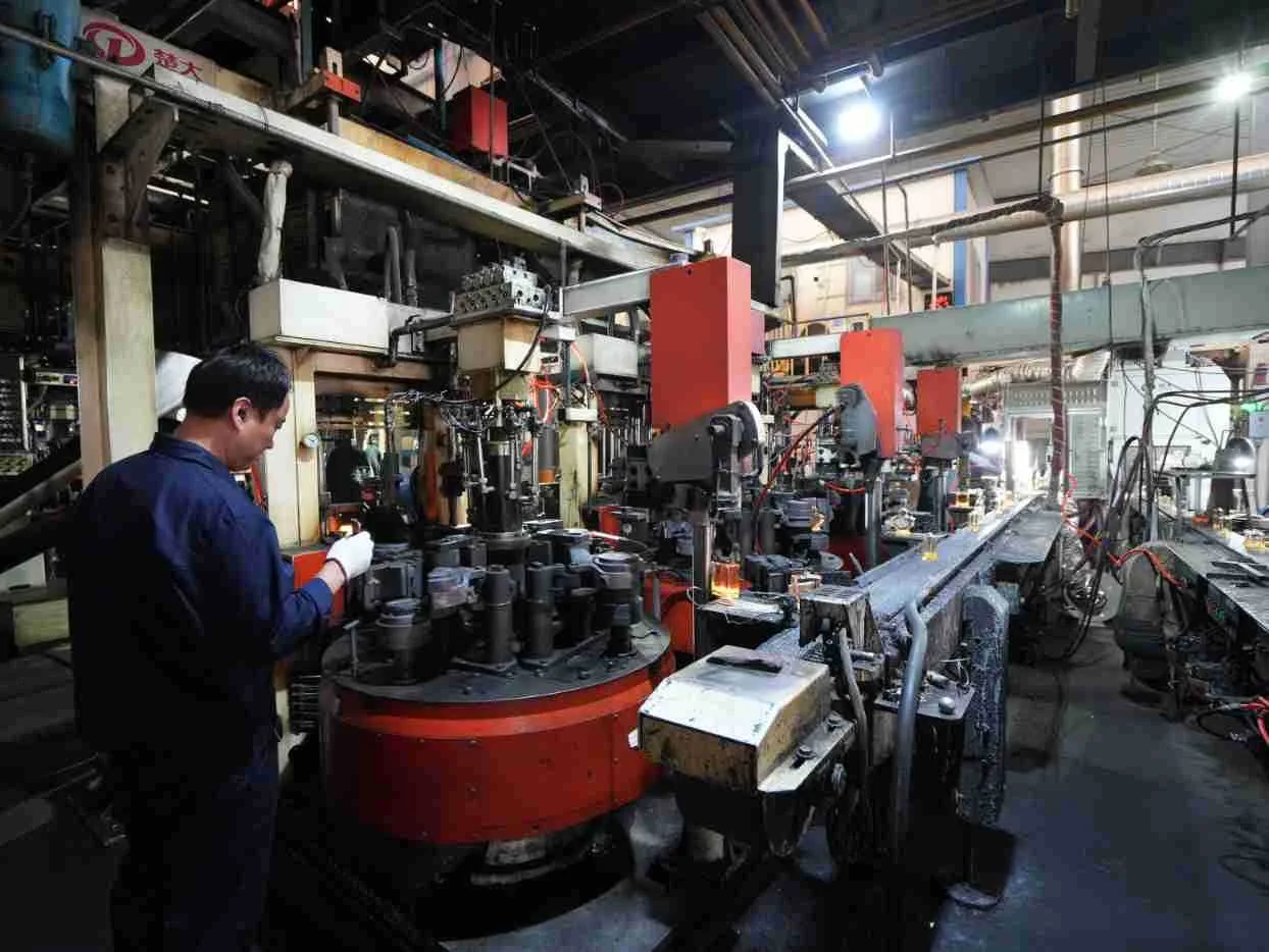 Factory operator monitoring glass bottle manufacturing equipment